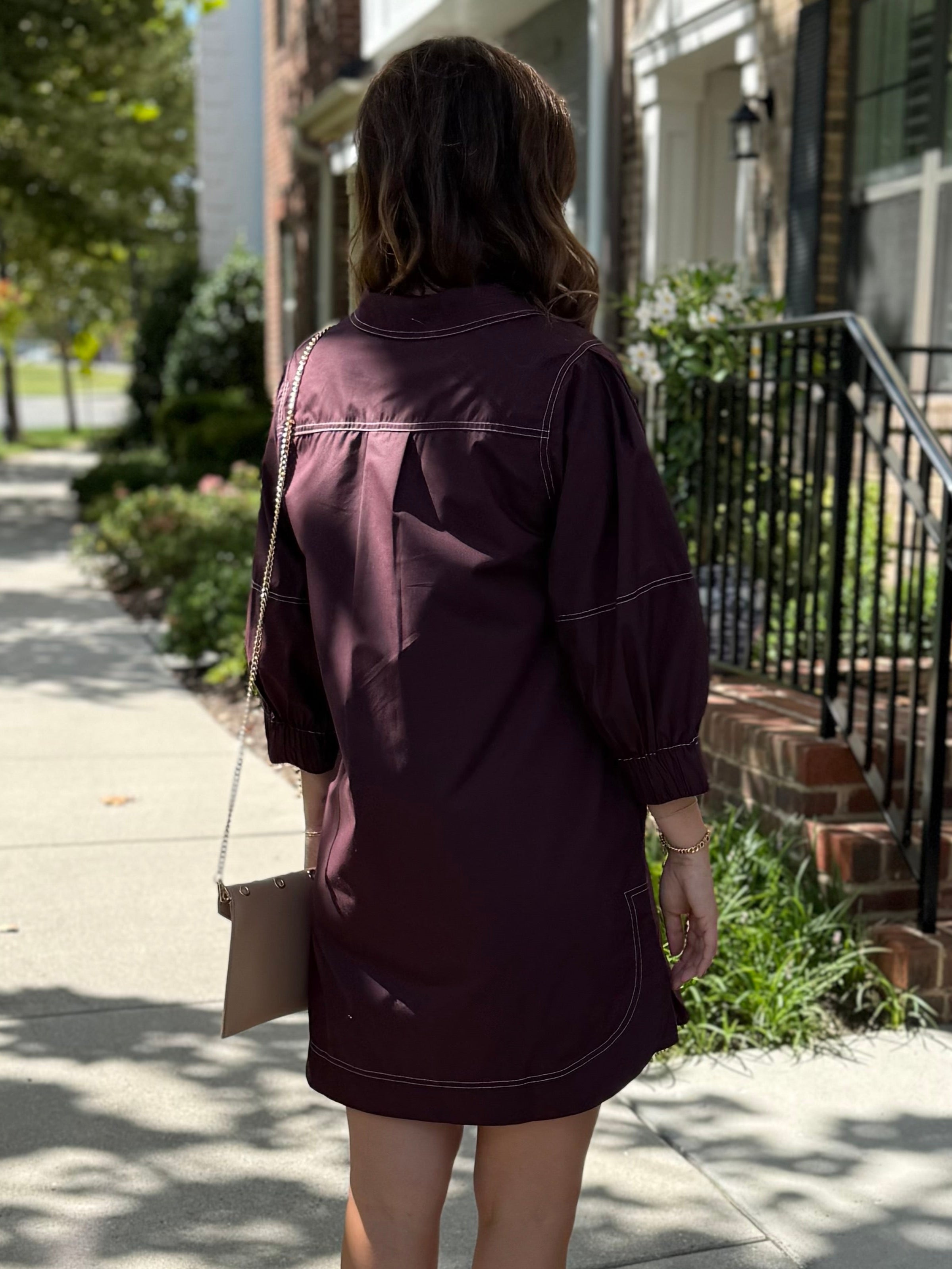 Woman in a brown dress walking on a sidewalk with a building in the background