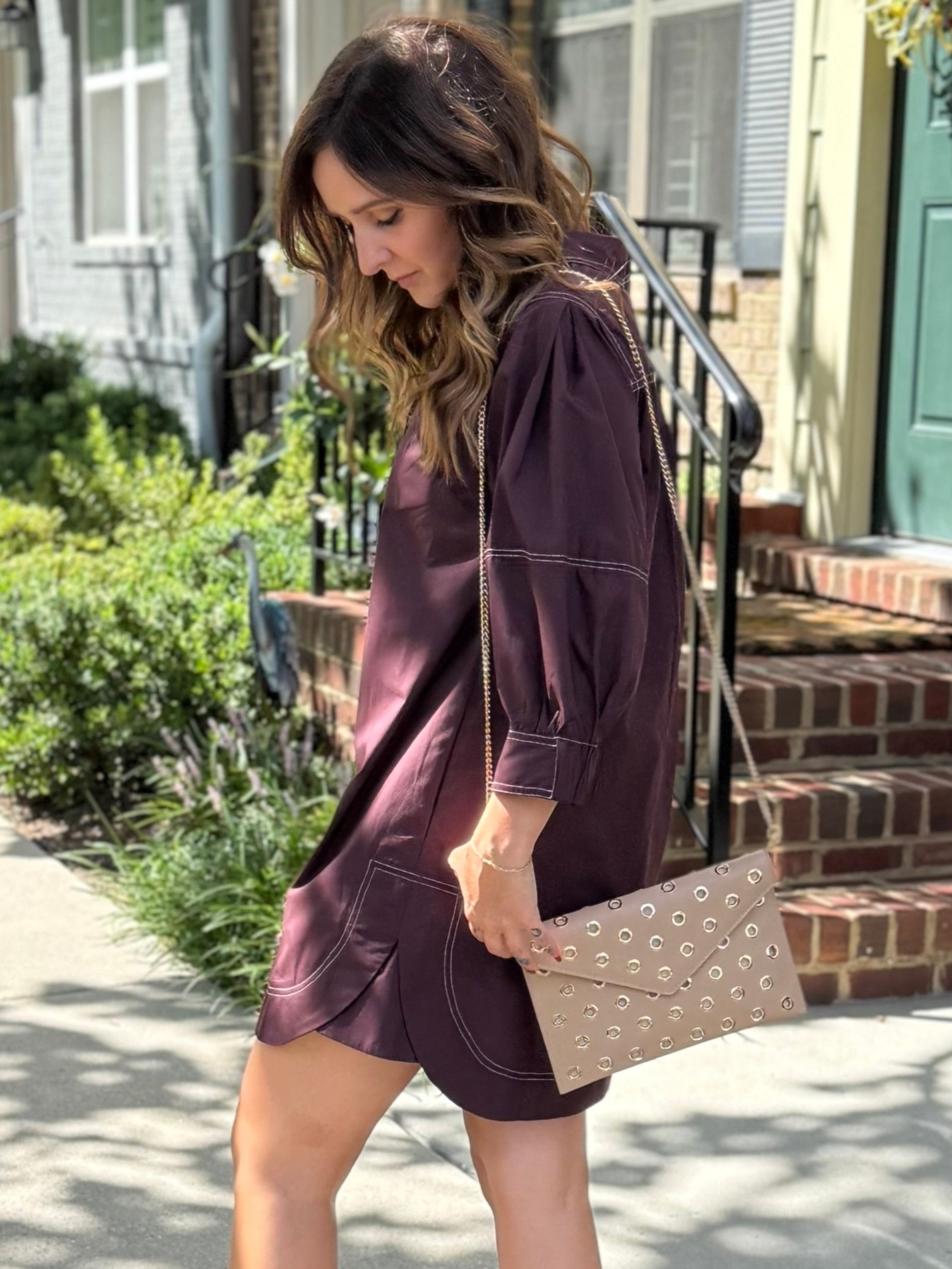 Woman in a brown dress holding a handbag on a sidewalk.