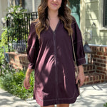 Woman in a brown dress standing on a sidewalk with a house in the background