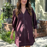 Woman in a brown dress standing on a sidewalk with a house in the background