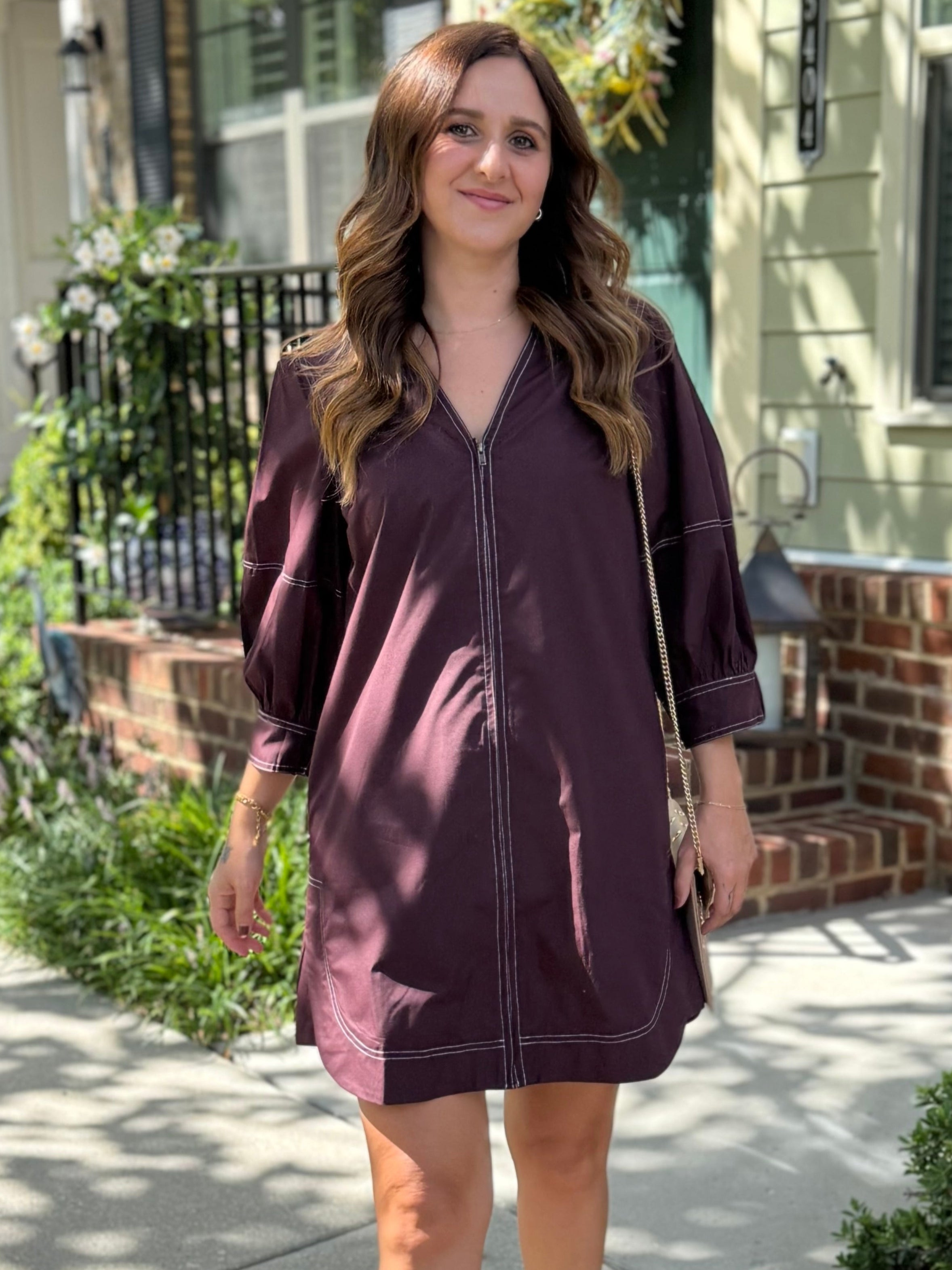 Woman in a brown dress standing on a sidewalk with a house in the background